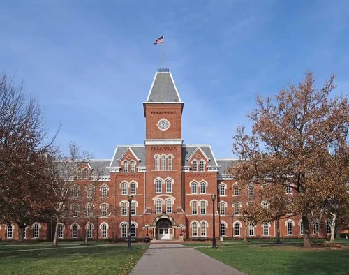 A brick building at Ohio State University with a clock tower, arched entryway, and fall trees under a clear blue sky.