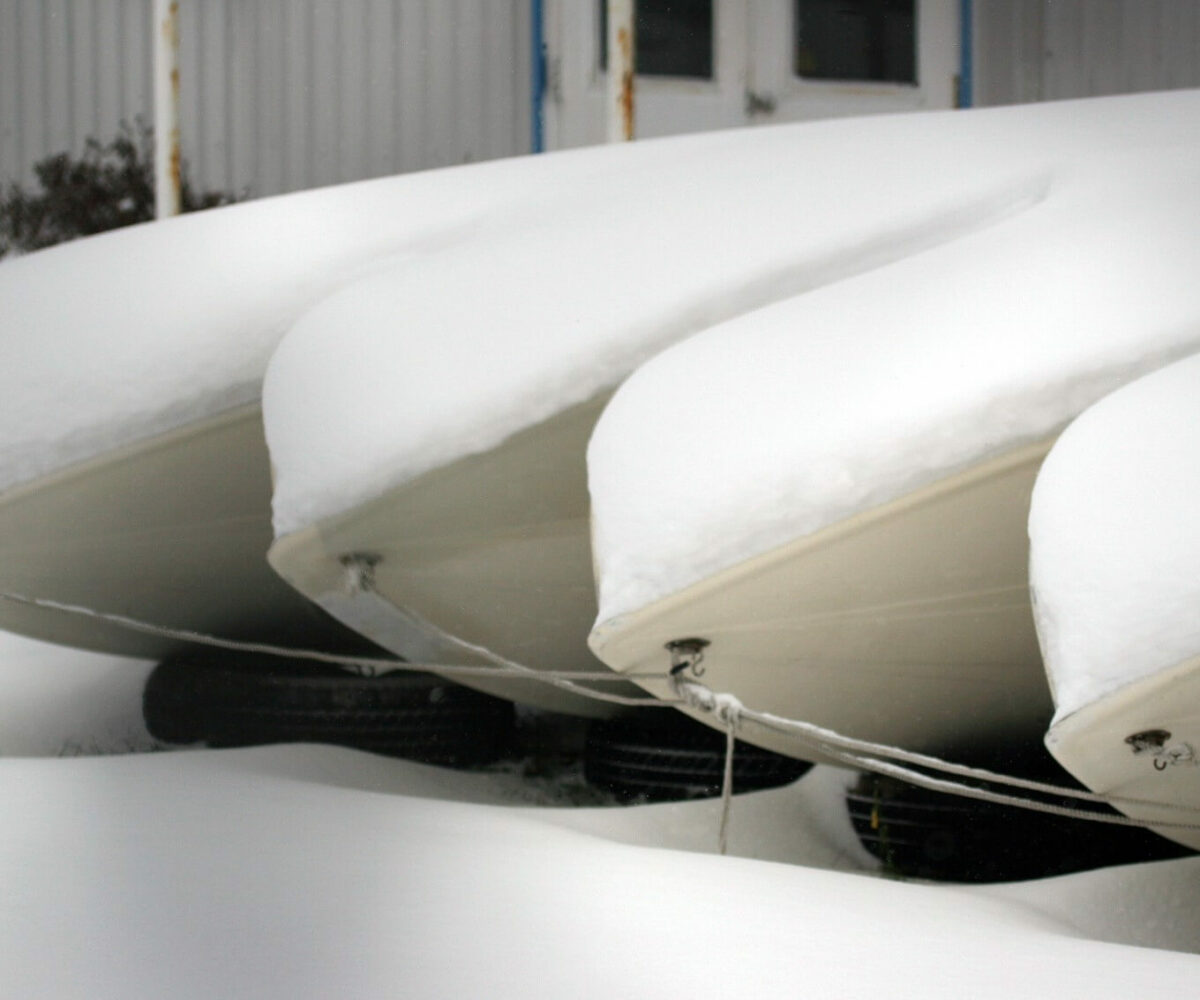 A row of boats sit in storage covered in snow