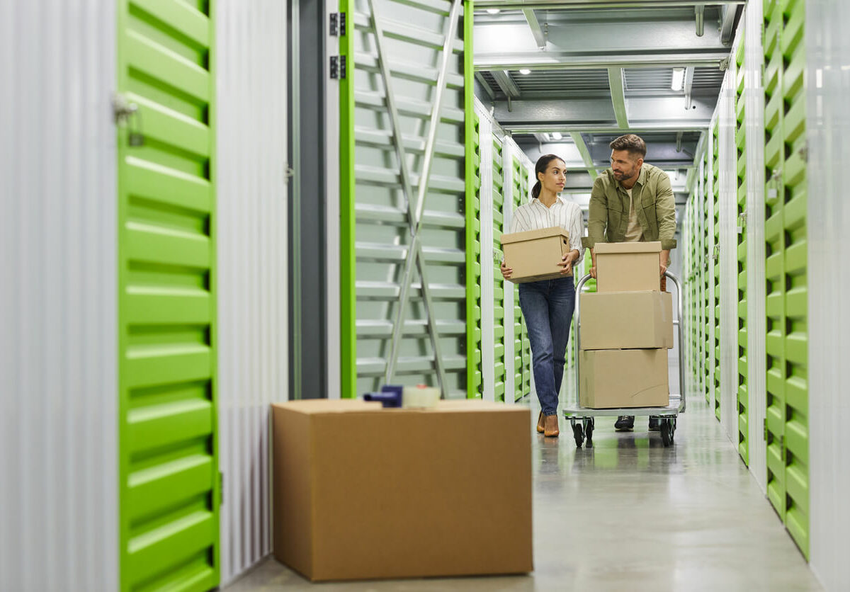 A couple bring boxes to their indoor storage unit on a moving cart.