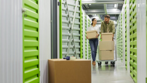 A couple bring boxes to their indoor storage unit on a moving cart.