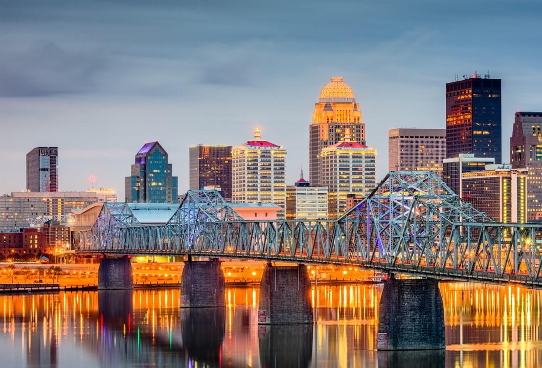 The Louisville skyline is illuminated against the Ohio River as the sun sets