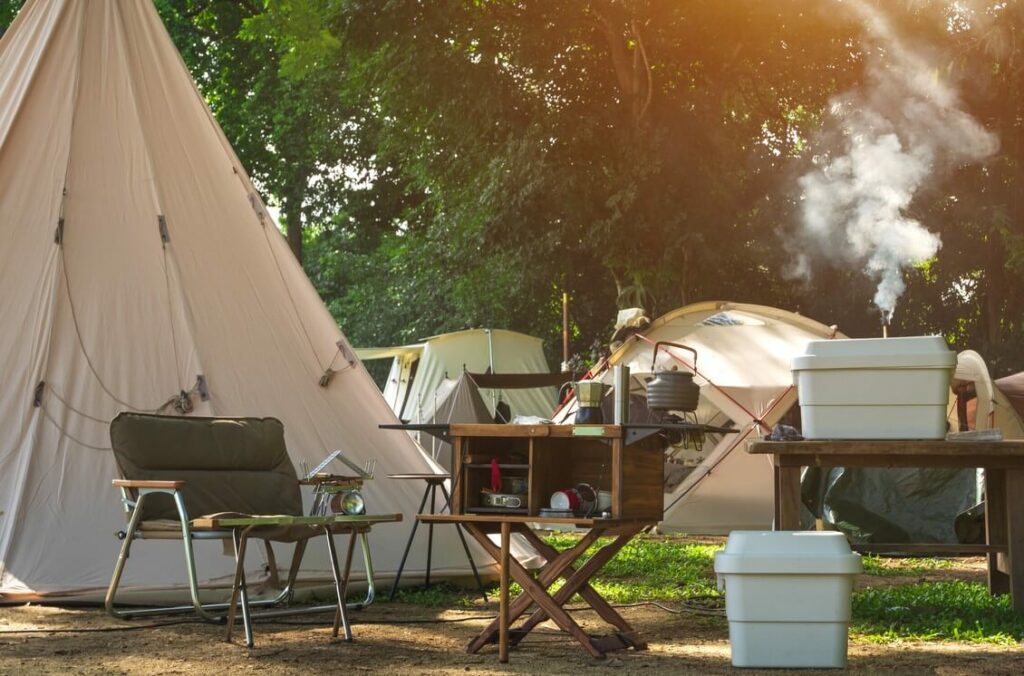 A quaint campsite in the woods, adorned with chairs, small tables, and more.