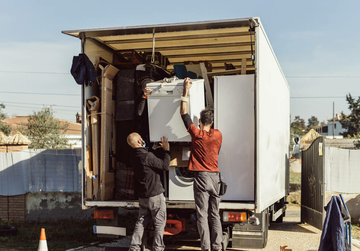 Two men moving a dishwasher into the back of a moving truck.