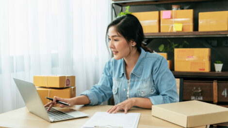 Woman sitting at a desk surrounded with cardboard boxes on a laptop