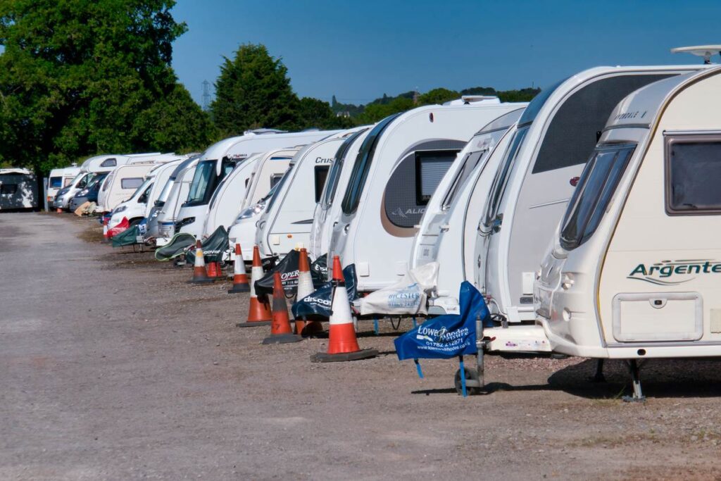White trailers and RVs are parked in a line in a parking lot on a sunny day.